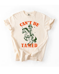 Ivory Can't Be Tamed Western heavyweight tee with distressed orange lettering and green cowgirl riding horse graphic.