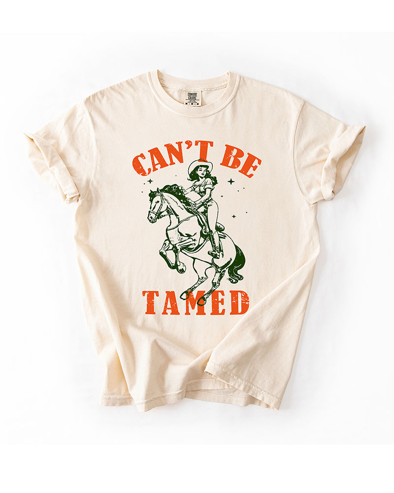 Ivory Can't Be Tamed Western heavyweight tee with distressed orange lettering and green cowgirl riding horse graphic.