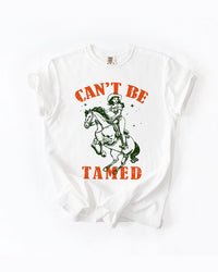 Woman modeling a White Can't Be Tamed cowgirl graphic tee with vintage horse artwork and black denim shorts.