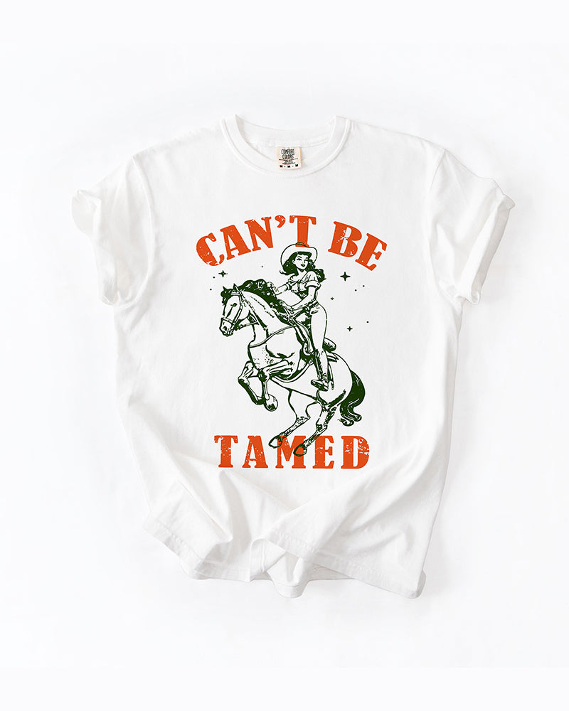 Woman modeling a White Can't Be Tamed cowgirl graphic tee with vintage horse artwork and black denim shorts.