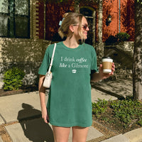 Woman holding coffee wearing I Drink Coffee Like A Gilmore tee in light green, Gilmore Girls fan shirt styled for fall