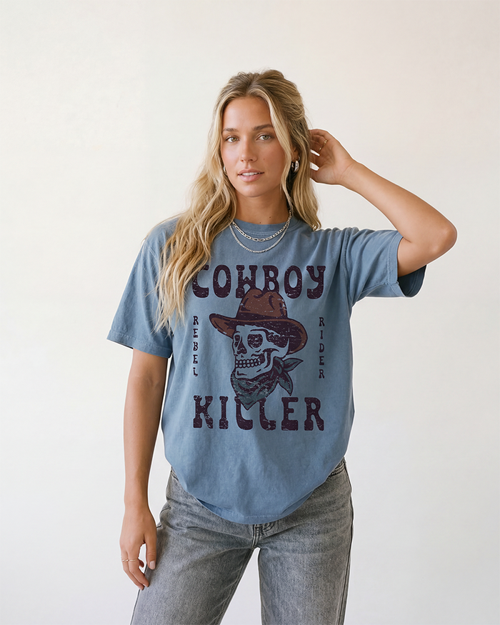 Woman wearing a Blue Jean Cowboy Killer Western graphic tee with cowboy skull artwork and grey jeans.