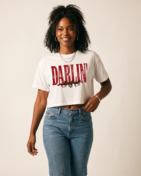 Woman wearing a white Darlin' Western horse crop top with distressed red lettering and running horses with blue jeans.