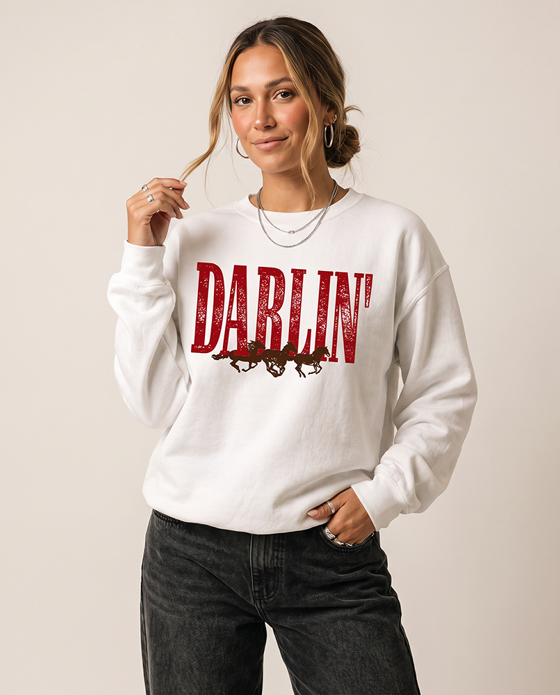 Woman modeling a white Darlin' Western horse crewneck sweatshirt with vintage distressed graphic and black jeans.