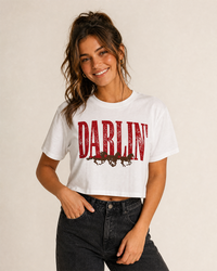 Woman wearing a white Darlin' Western graphic crop top featuring distressed red lettering and brown running horses.