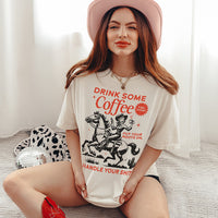 Model in ivory graphic tee styled with cowboy hat and boots — caffeine-fueled cowgirl outfit