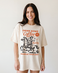 Woman wearing an ivory heavyweight cowgirl coffee tee featuring a vintage Western horse graphic and distressed lettering.