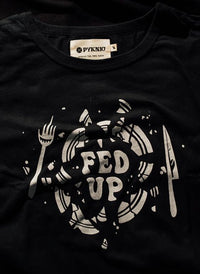 Flatlay of Fed Up graphic tee on black background. Broken plate design and bold lettering centered on black shirt.