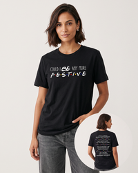 Brunette woman wearing a black Friends Christmas graphic tee with gray denim jeans, featuring colorful logo-inspired lettering and Christmas quotes on the back.