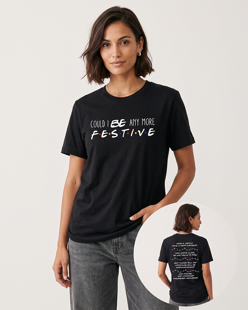 Brunette woman wearing a black Friends Christmas graphic tee with gray denim jeans, featuring colorful logo-inspired lettering and Christmas quotes on the back.
