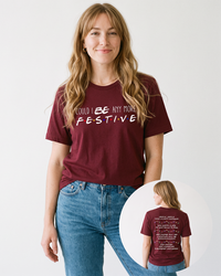 Blonde woman wearing a maroon Could I Be Any More Festive Christmas T-shirt with blue denim jeans, showing the Friends-inspired front and back graphics.