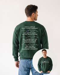 Male model wearing a forest green Friends-inspired Christmas crewneck sweatshirt with blue jeans, showing Phoebe's holiday song on the back and festive front lettering in the inset.