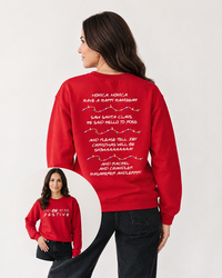 Brunette woman wearing a red Could I Be Any More Festive Christmas sweatshirt with black denim jeans, featuring colorful holiday lights and Friends-inspired song lyrics on the back.