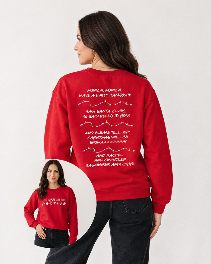 Brunette woman wearing a red Could I Be Any More Festive Christmas sweatshirt with black denim jeans, featuring colorful holiday lights and Friends-inspired song lyrics on the back.