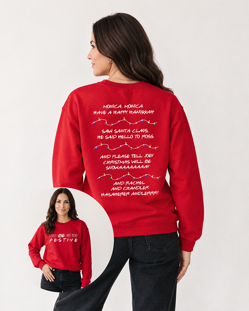 Brunette woman wearing a red Could I Be Any More Festive Christmas sweatshirt with black denim jeans, featuring colorful holiday lights and Friends-inspired song lyrics on the back.