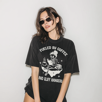 Model wearing Fueled by Coffee and Cliffhangers tee in black — skeleton reading shirt for caffeine-addicted readers