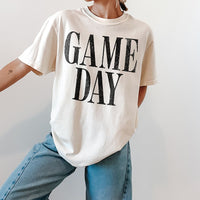 Woman wearing ivory Game Day heavyweight tee with jeans and sneakers — casual unisex sports shirt for everyday wear.