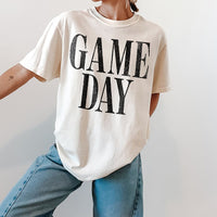 Woman wearing ivory Game Day heavyweight tee with jeans and sneakers — casual unisex sports shirt for everyday wear.