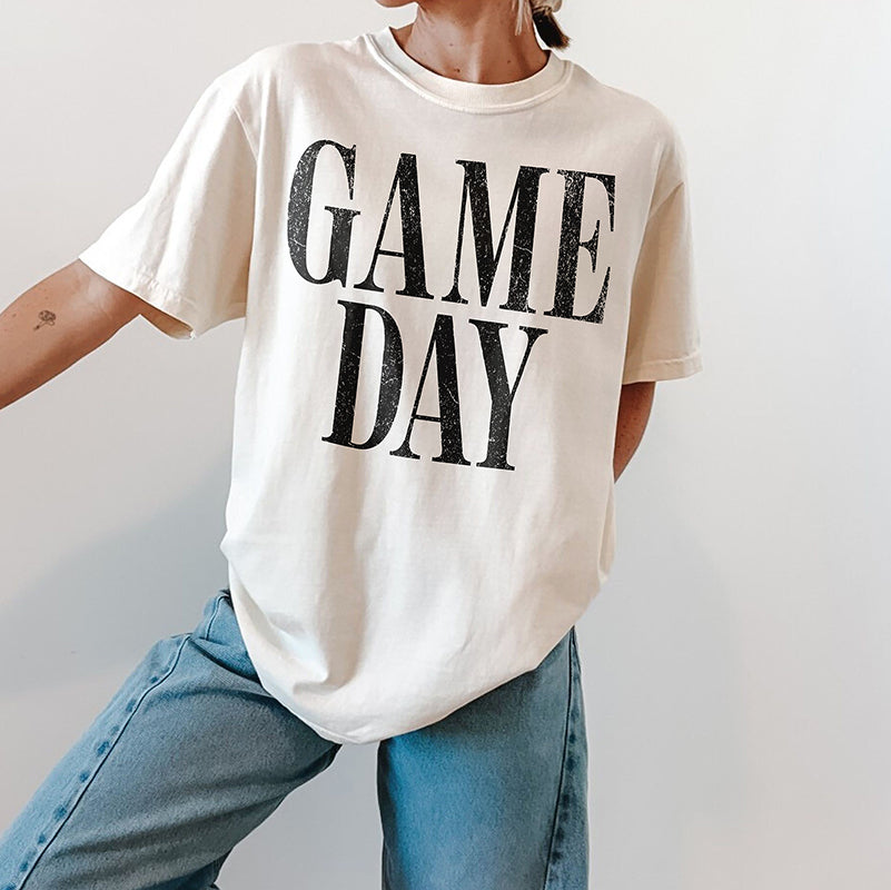 Woman wearing ivory Game Day heavyweight tee with jeans and sneakers — casual unisex sports shirt for everyday wear.
