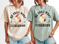 Side-by-side image of ivory and bay vintage Santa book lover tees – Christmas shirt for readers and cozy holiday gifting