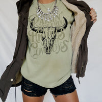 Model wearing khaki Raisin’ Hell tee — earthy toned cowgirl and hippie fusion t-shirt