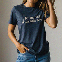 Woman wearing the I Put My Book Down To Be Here Tee in heather navy – funny book lover t-shirt with witty reading quote.