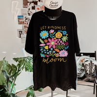 Flat lay of Let Kindness Bloom tee in black — bright multicolor floral design on vintage-style shirt