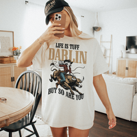 Woman wearing Life Is Tuff Darlin tee and baseball-style cowboy hat — selfie style, country western look