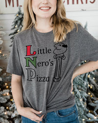 Woman wearing a heather gray Little Nero's Pizza lightweight Christmas graphic tee with jeans near decorated Christmas trees.