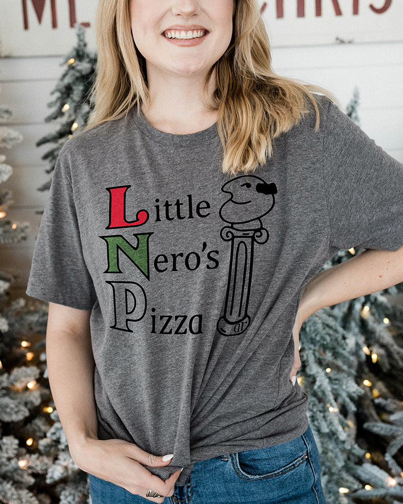 Woman wearing a heather gray Little Nero's Pizza lightweight Christmas graphic tee with jeans near decorated Christmas trees.