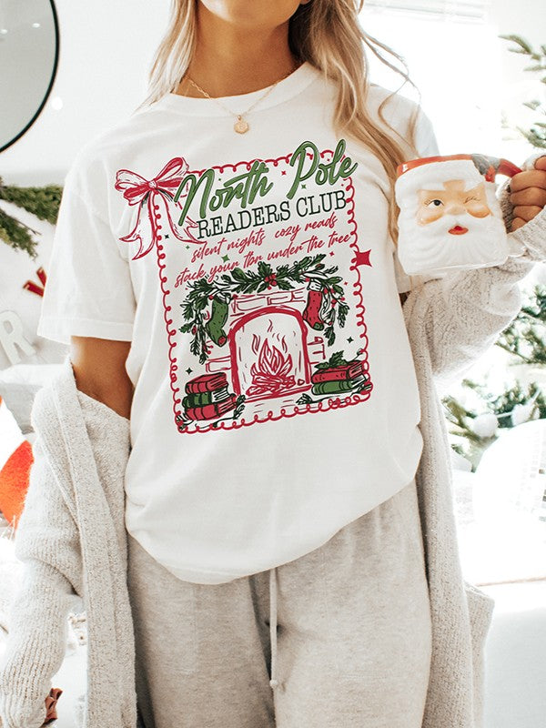 Woman wearing heavyweight vintage-style Christmas tee for book lovers — North Pole Readers Club design with greenery and fireplace