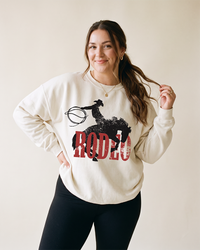 Woman wearing a bone Rodeo Western heavyweight crewneck sweatshirt with distressed cowboy and bucking horse graphic.