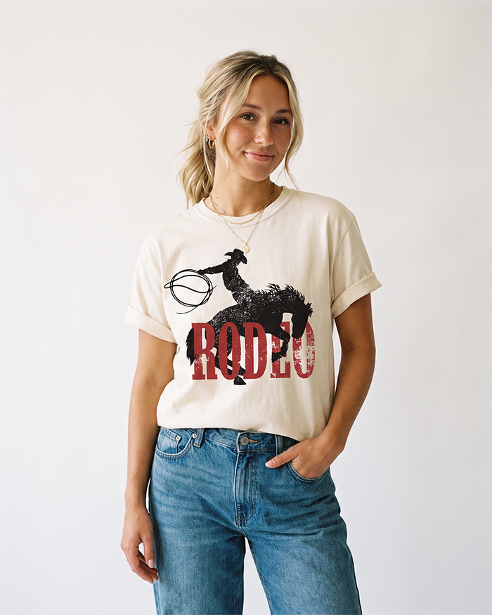 Woman wearing an ivory Western rodeo heavyweight T-shirt with distressed cowboy and horse graphic and blue jeans.