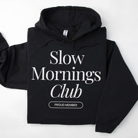 Flatlay of black Slow Mornings Club hoodie featuring cozy coffee-inspired graphic design