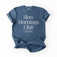 Flatlay of denim blue Slow Mornings Club Tee with cozy slow living graphic design