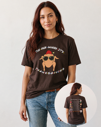 Brunette woman wearing a brown Friends-inspired Thanksgiving graphic tee with blue jeans, showing the turkey front print and Thanksgiving episode artwork on the back.