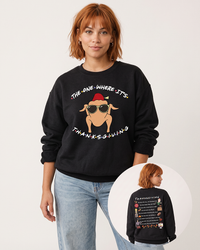 Red-haired woman wearing a black Friends Thanksgiving crewneck sweatshirt with light blue denim, featuring the turkey in sunglasses and illustrated back print.