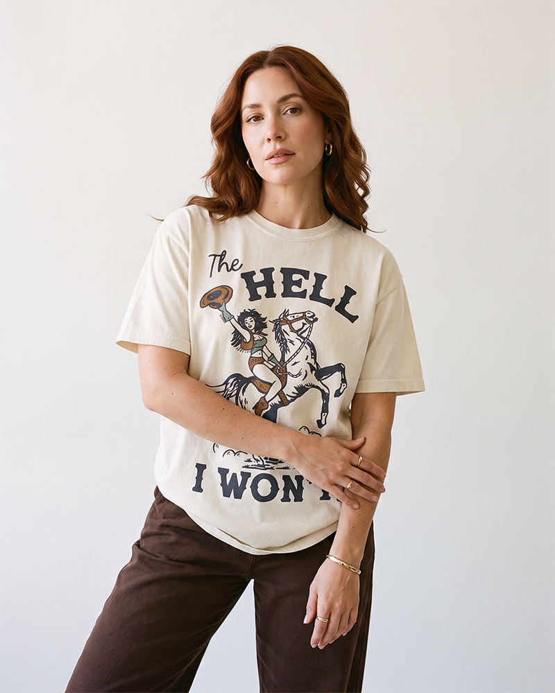 Woman wearing an ivory Western graphic tee featuring a cowgirl on horseback and The Hell I Won't lettering.