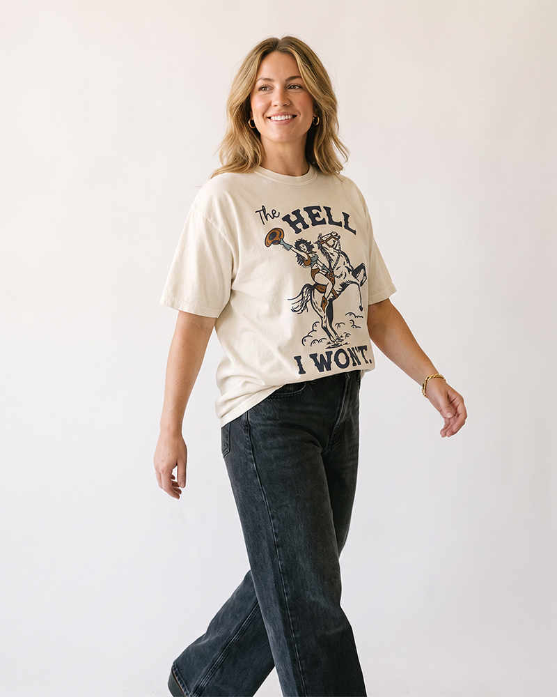Woman modeling an ivory heavyweight cowgirl graphic tee with The Hell I Won't horse artwork.