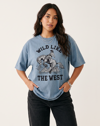 Woman wearing a Blue Jean Wild Like The West Western graphic tee featuring a cowboy riding a bucking horse with black jeans.