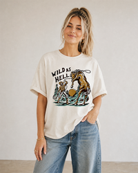 Woman modeling an ivory Wild As Hell heavyweight tee featuring a vintage cowboy, rearing horse and desert design.