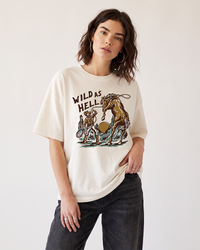 Woman wearing an ivory Wild As Hell Western graphic tee with cowboy and wild horse artwork and black jeans.