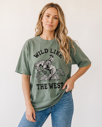 Woman modeling a Sage Wild Like The West cowboy graphic tee with vintage bucking horse artwork and blue jeans.