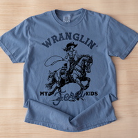 Flat lay of blue jean Wranglin’ My Feral Kids tee — funny cowgirl tee for moms