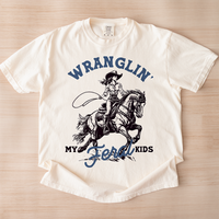 Flat lay of Wranglin’ My Feral Kids tee in ivory — western motherhood shirt