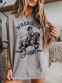 Model wearing Wranglin’ My Feral Kids tee in grey — funny western mom graphic t-shirt
