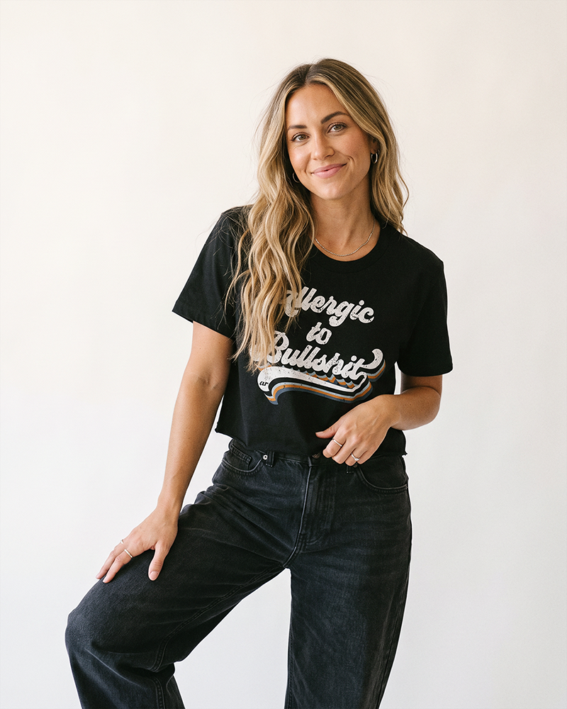 Blonde woman wearing black Allergic to Bullshit crop top with high waisted black jeans
