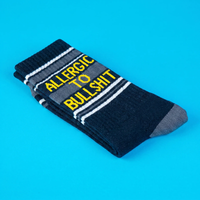 Folded black Allergic To Bullshit socks with yellow lettering and white retro stripes