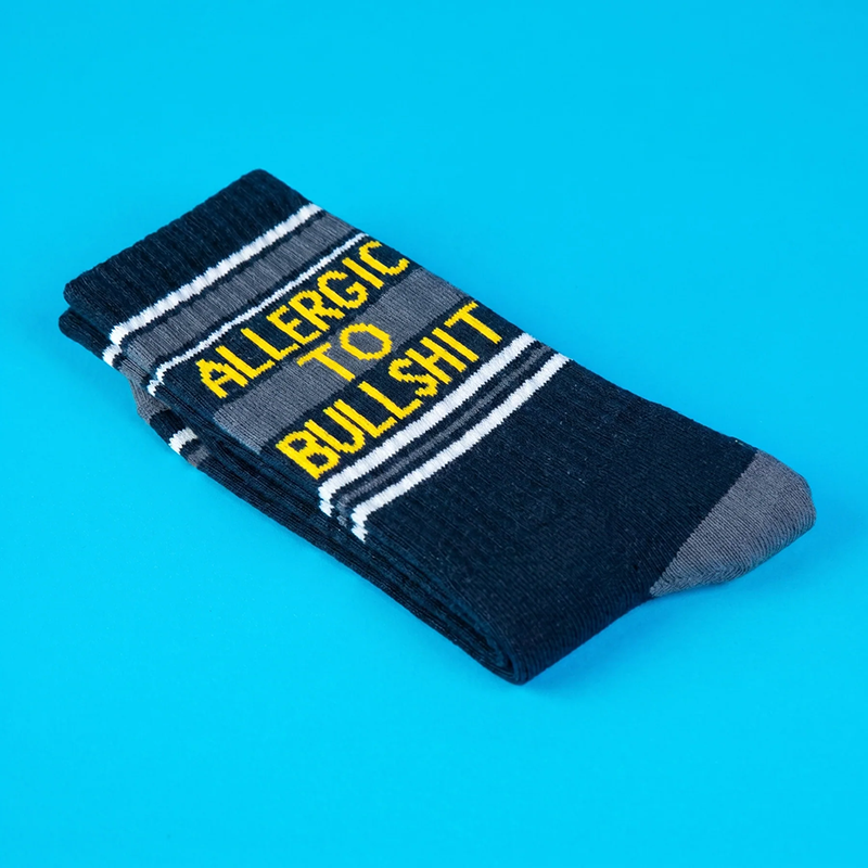 Folded black Allergic To Bullshit socks with yellow lettering and white retro stripes