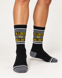 Woman wearing black Allergic To Bullshit gym socks with yellow lettering and gray striped details
